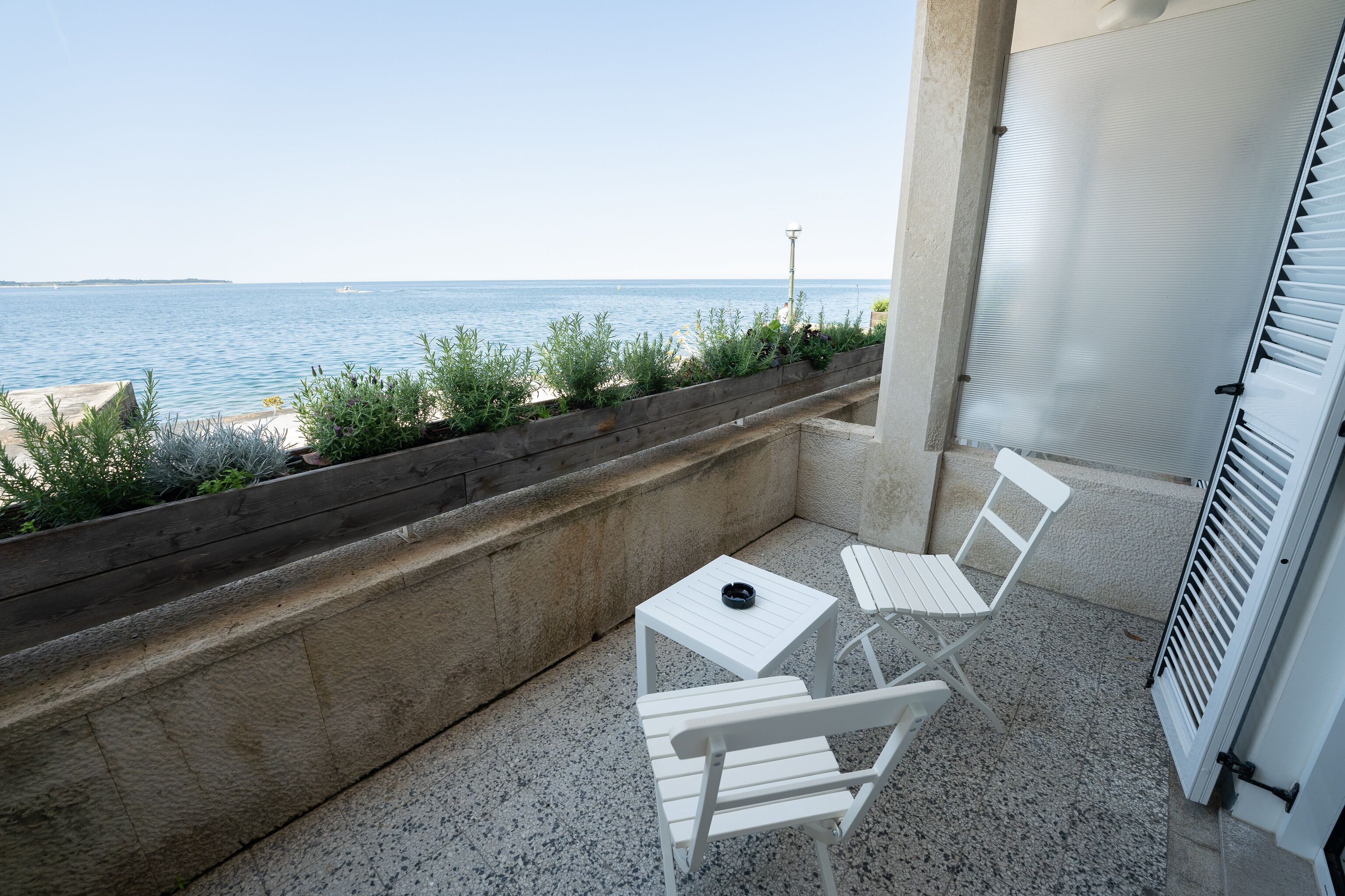 A balcony with two white chairs, a small table, and a view of the sea.