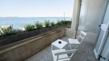 A balcony with two white chairs, a small table, and a view of the sea.