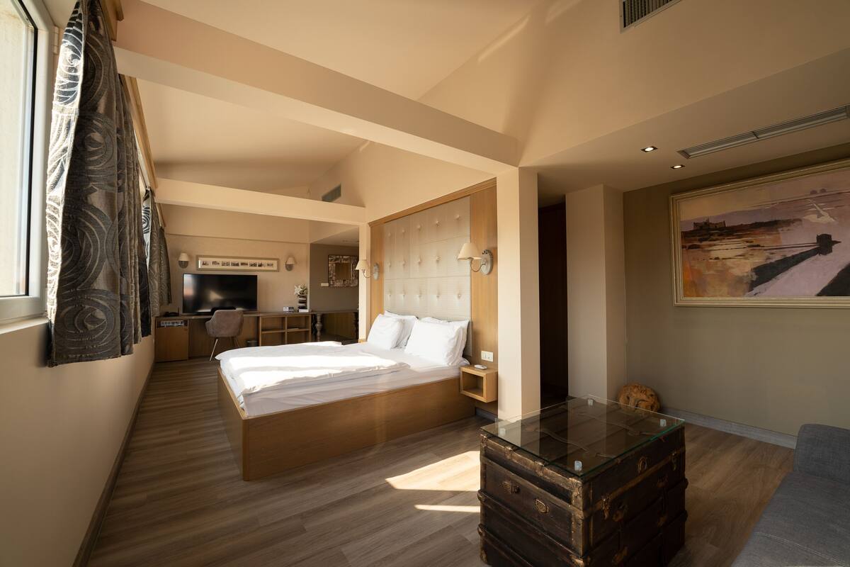 A modern hotel room with a large bed, a glass coffee table, a desk, and a television.