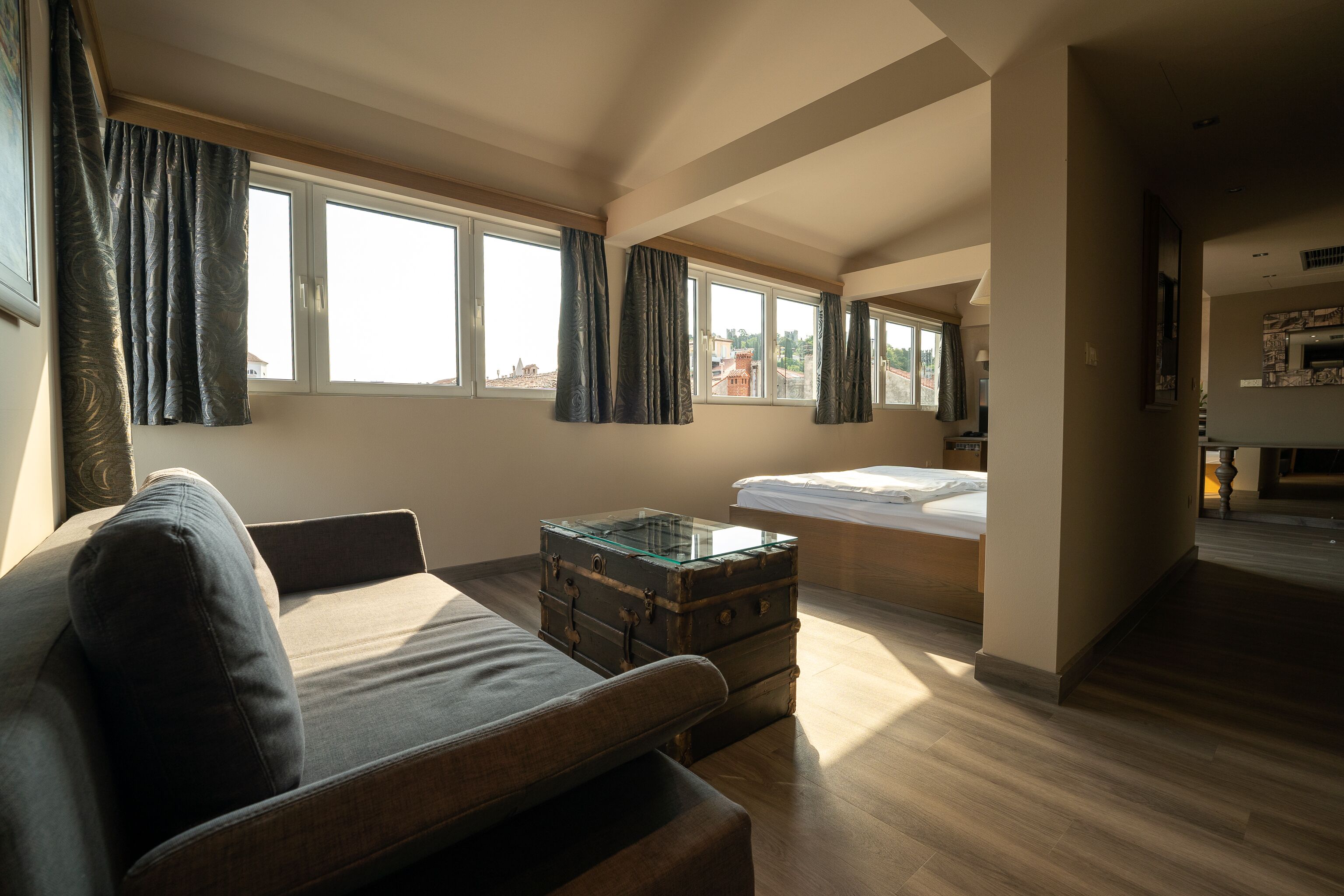 A spacious room with a large window, a sofa, a bed, and a wooden floor.