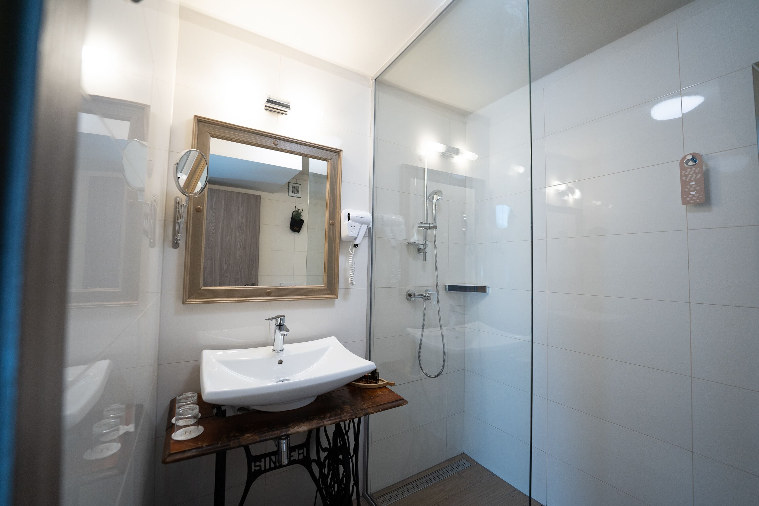 Ein modernes Badezimmer mit einem weißen Waschbecken, einem Holzlagerraum, einem Spiegel und einer Duschkabine aus Glas.