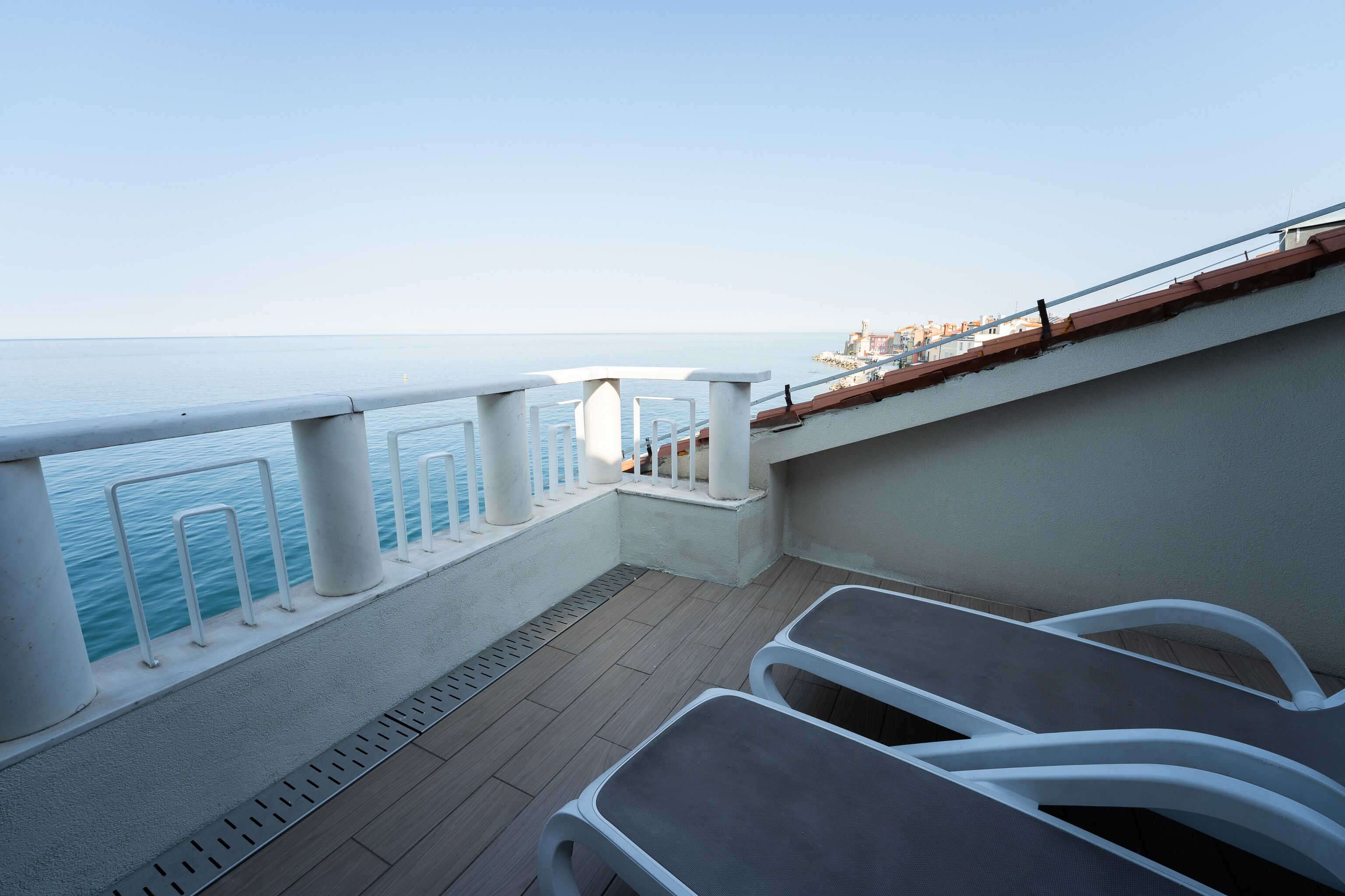 Terraza con vistas al mar, barandillas blancas y algunas sillas.