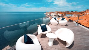 A rooftop terrace with white modern seating and a glass balustrade overlooking the sea. - Hotel Piran (Piran)