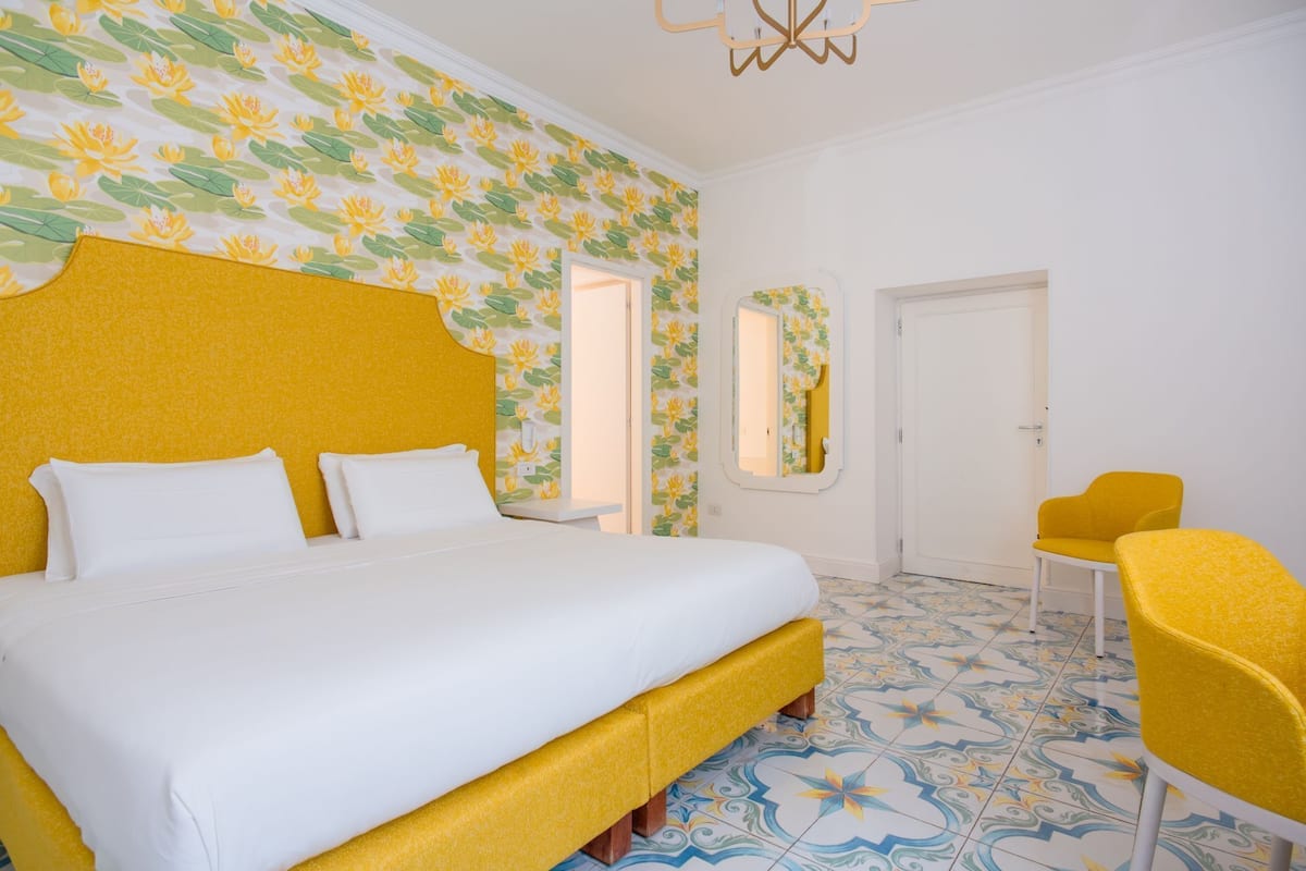 A hotel room with a large bed, a yellow armchair, and a mirror on the wall.