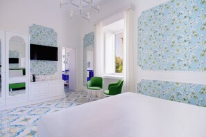 Un dormitorio con una cama grande, una silla verde, un televisor y un baño visible a través de una puerta abierta.
