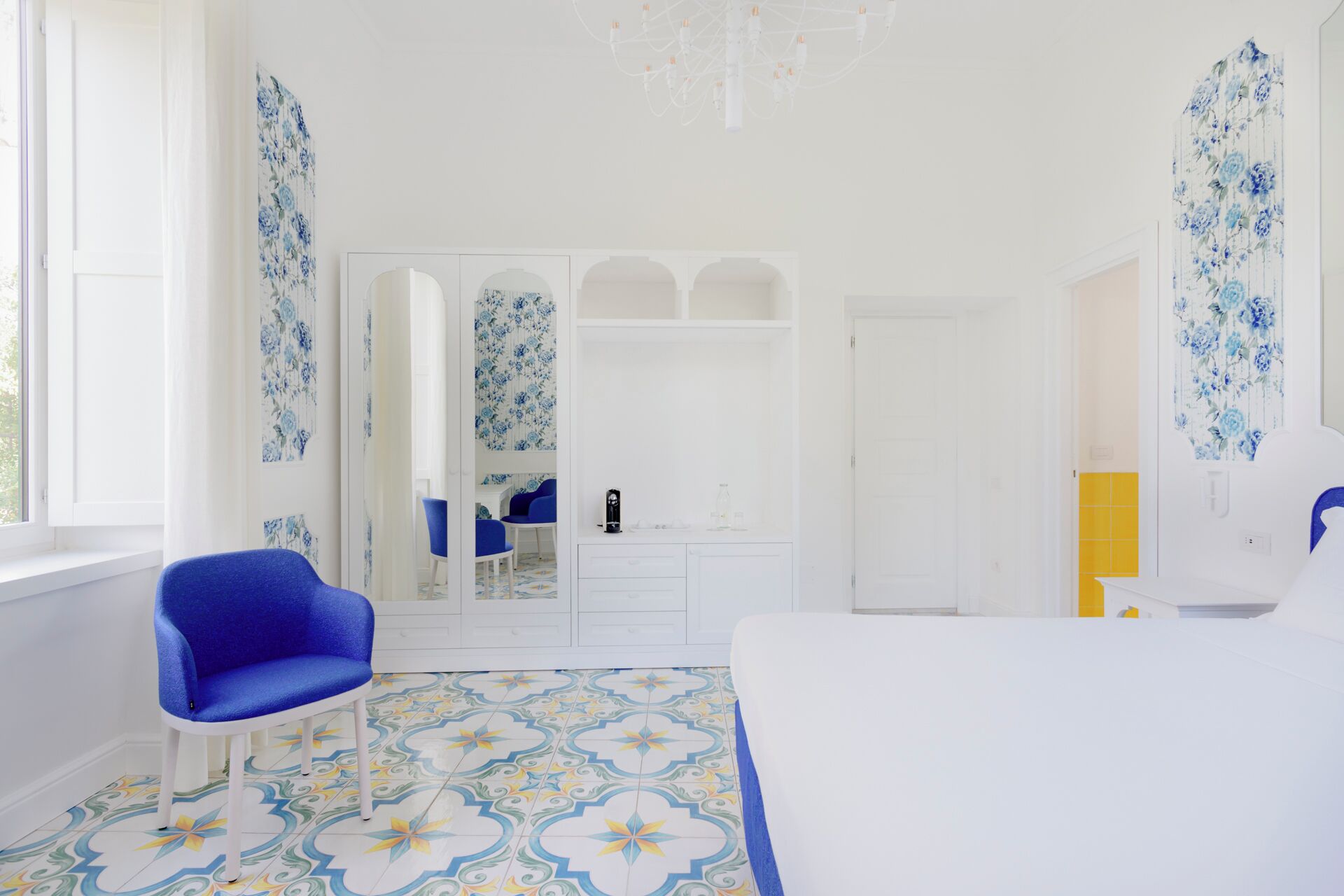 A bedroom with a bed, a blue chair, a wardrobe, and a mirror.