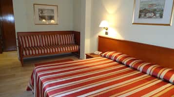 Ein Hotelzimmer mit Bett, einem gestreiften Sofa, einem Nachttisch mit Lampe und gerahmten Bildern an den Wänden.