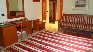 A hotel room with a wooden desk, a striped sofa, a large mirror, and a framed picture on the wall. - Hotel Select (Montecchio Emilia)