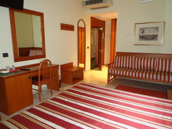 A hotel room with a wooden desk, a striped sofa, a large mirror, and a framed picture on the wall. - Hotel Select (Montecchio Emilia)