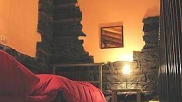 A room with a stone wall, a bed with a red cover, and a stone fireplace.
