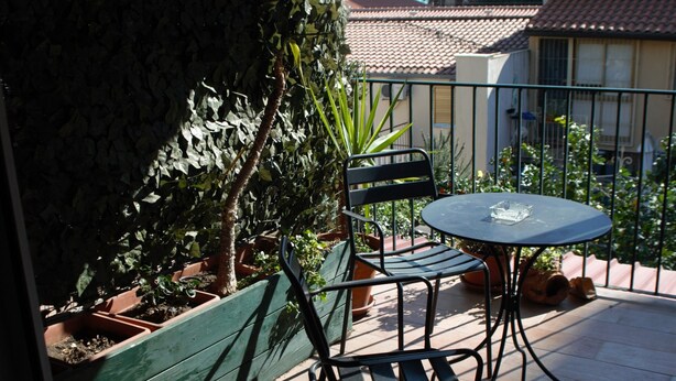Un balcon avec une table et des chaises, entouré de plantes en pot et offrant une vue sur les bâtiments.