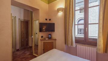 A hotel room with a bed, a TV mounted on the wall, a window with curtains, and a door leading to another room.