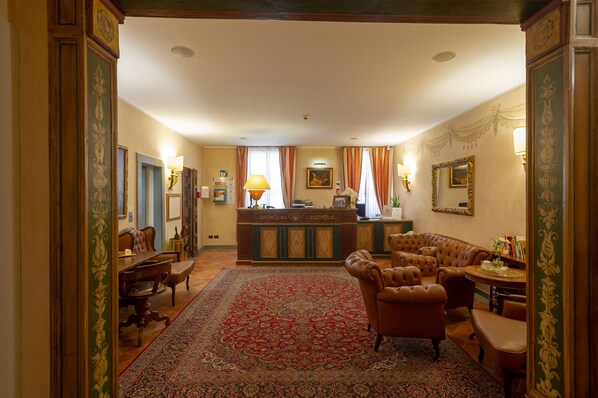 A traditional hotel lobby with a reception desk, seating area, and ornate decor.