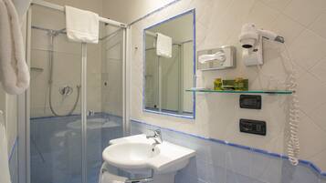 Un baño con cabina de ducha de vidrio, un lavabo, un espejo y un secador de pelo montado en la pared.