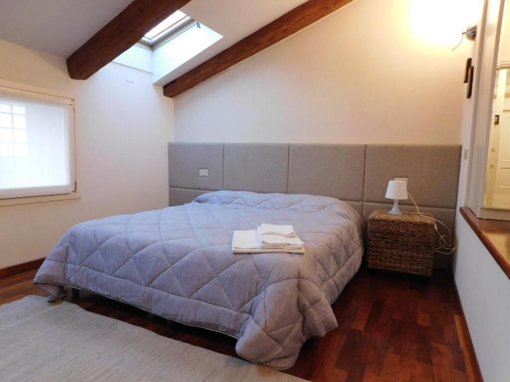 A bedroom with a bed, a headboard, a bedside table with a lamp, a window, and a skylight.
