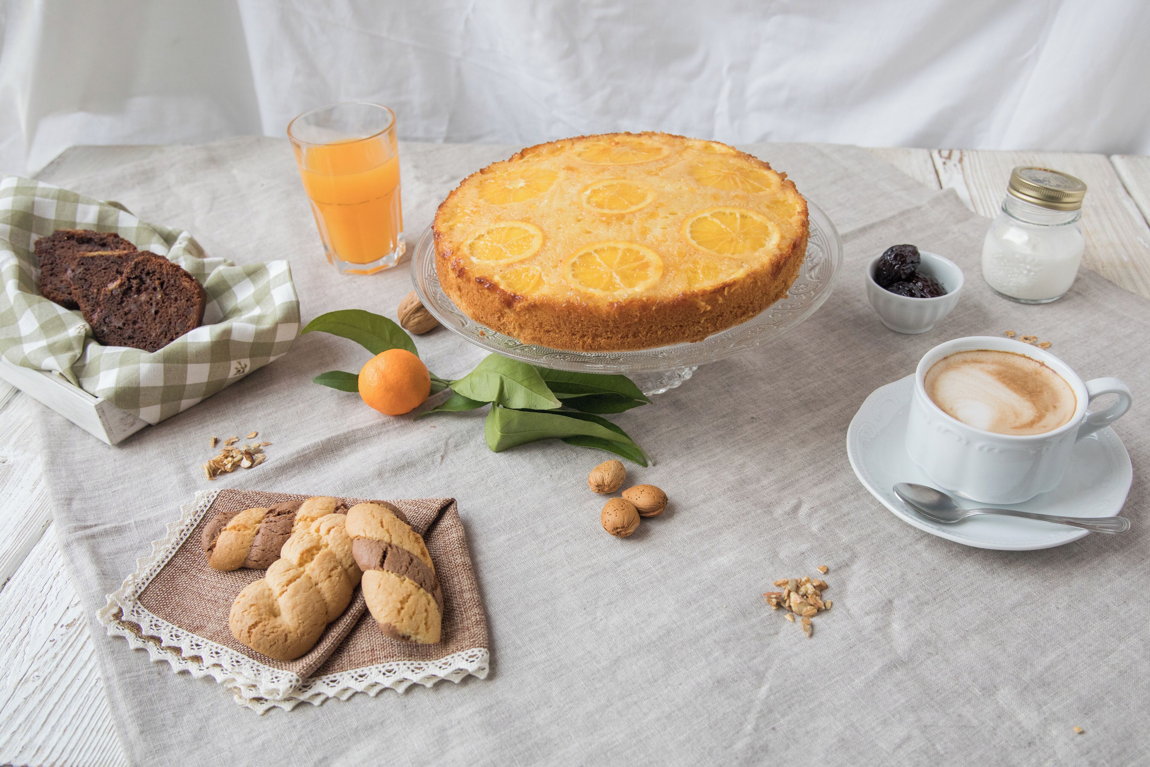 A breakfast setting with a cake, cookies, coffee, and a glass of orange juice on a table.