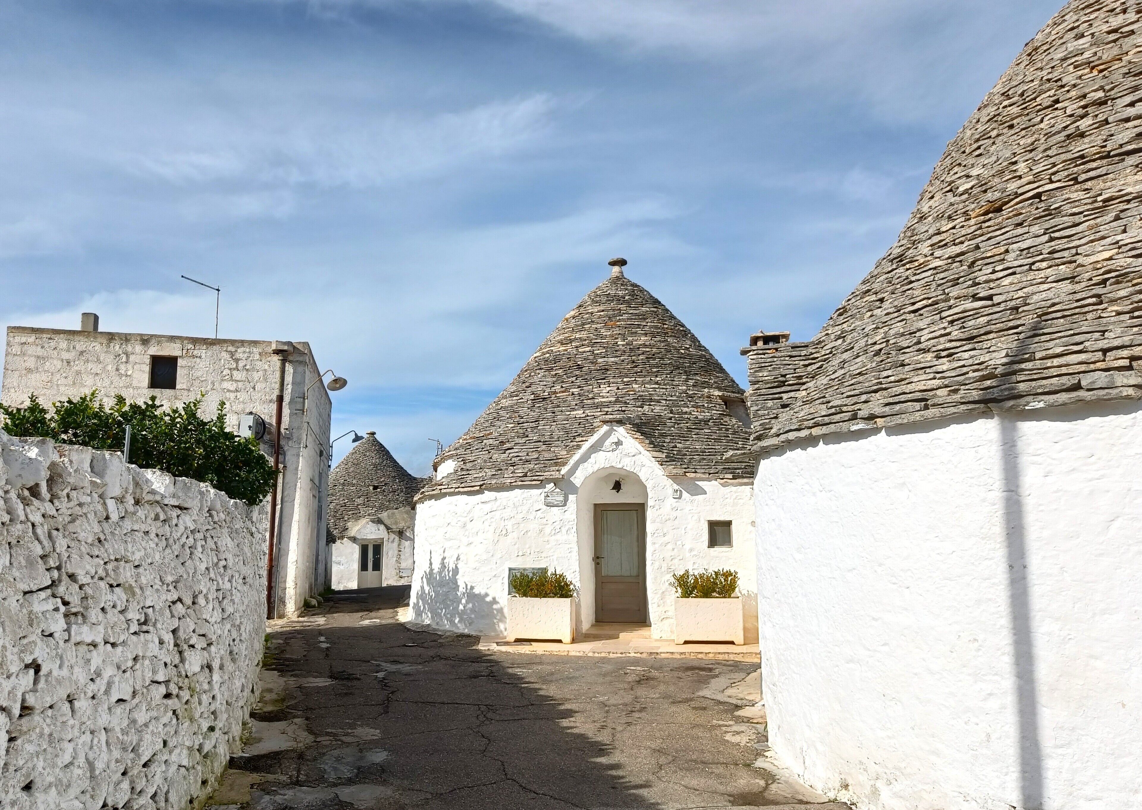 A narrow street lined with traditional stone-roofed buildings, white walls, and a clear sky.