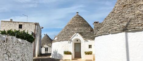 A narrow street lined with traditional stone-roofed buildings, white walls, and a clear sky.