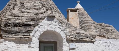 A traditional stone house with a conical roof, a small arched entrance, and a door with a window above it.