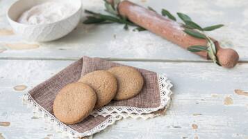 Un décor rustique avec une table en bois sur laquelle sont disposés des biscuits sur un chemin de table en dentelle, un rouleau à pâtisserie et un bol de farine.