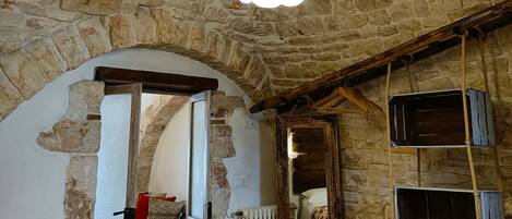 A rustic room with exposed stone walls, a wooden ceiling, and a bed with a patterned bedspread.