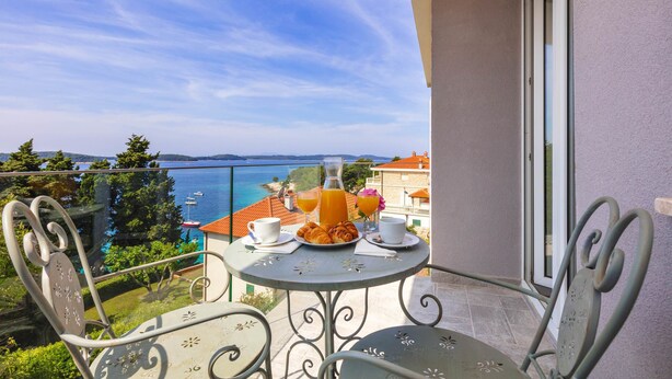 A balcony with a table set for breakfast, overlooking a scenic view of the sea and buildings. - Aparthotel Pharia (Hvar)