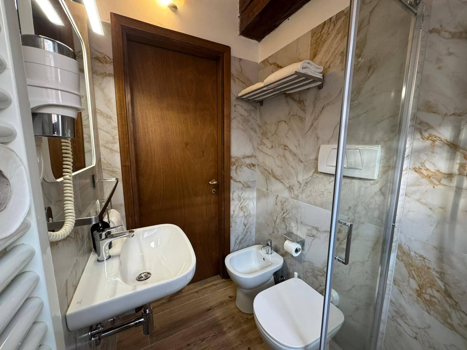 A bathroom with a wooden door, a sink, a bidet, and a glass shower enclosure.