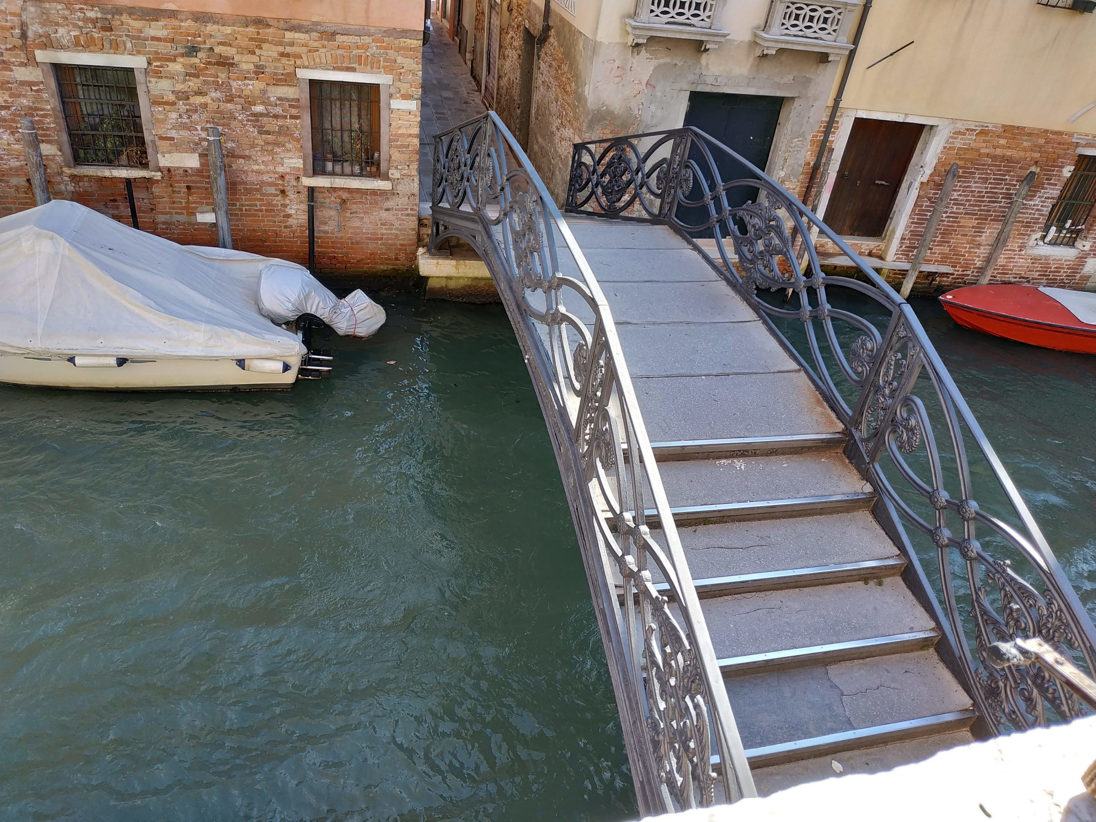 A narrow bridge with ornate metal railings connecting two buildings over a canal.