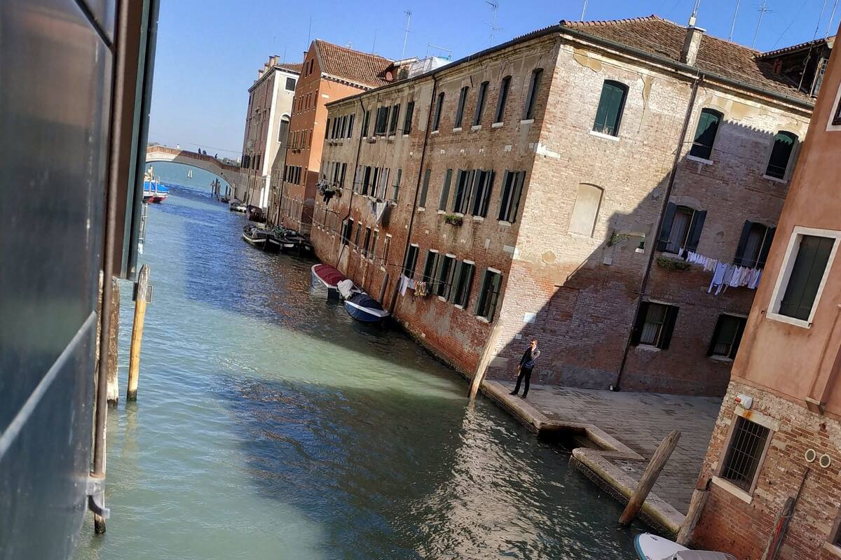 A narrow canal with boats docked on the right, surrounded by historic buildings with visible balconies and windows.