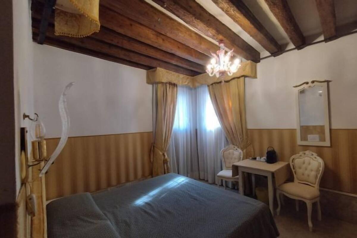 A room with a bed, a desk, a chair, a mirror, and a chandelier.