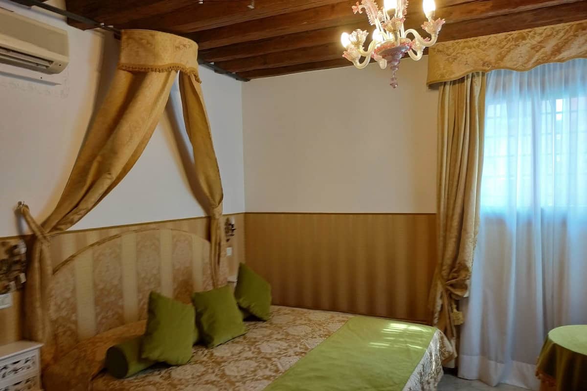 A bedroom with a bed, green pillows, a chandelier, and curtains.
