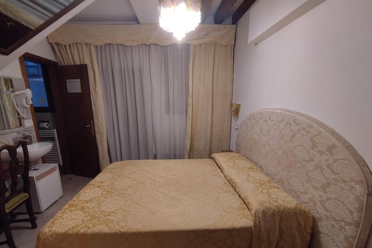 A bedroom with a bed, a desk, a chair, a mirror, a nightstand, and a window with curtains.