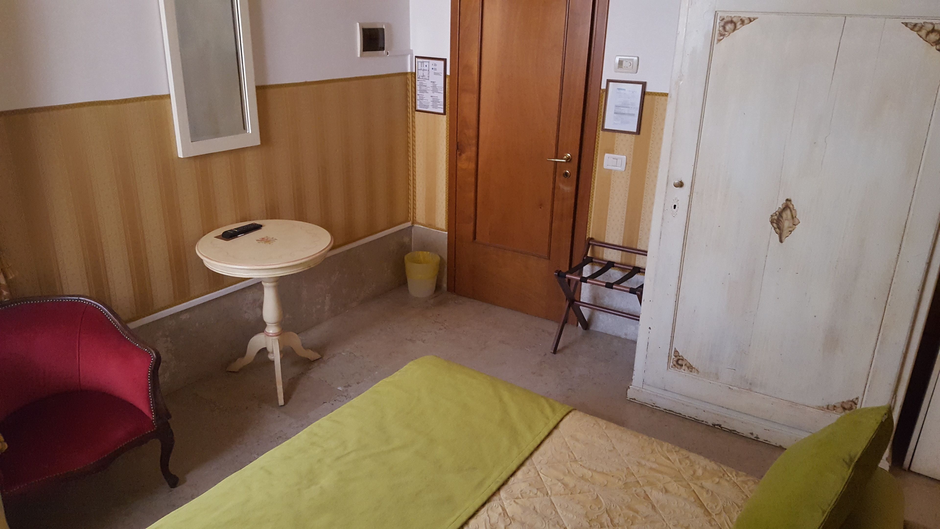 Une petite pièce, de taille modeste, comprenant une table ronde, une chaise rouge, un lit vert et une armoire blanche.