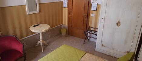 Une petite pièce, de taille modeste, comprenant une table ronde, une chaise rouge, un lit vert et une armoire blanche.