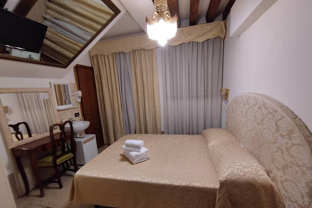 A hotel room with a bed, a desk with a chair, a sink, and a mirror.