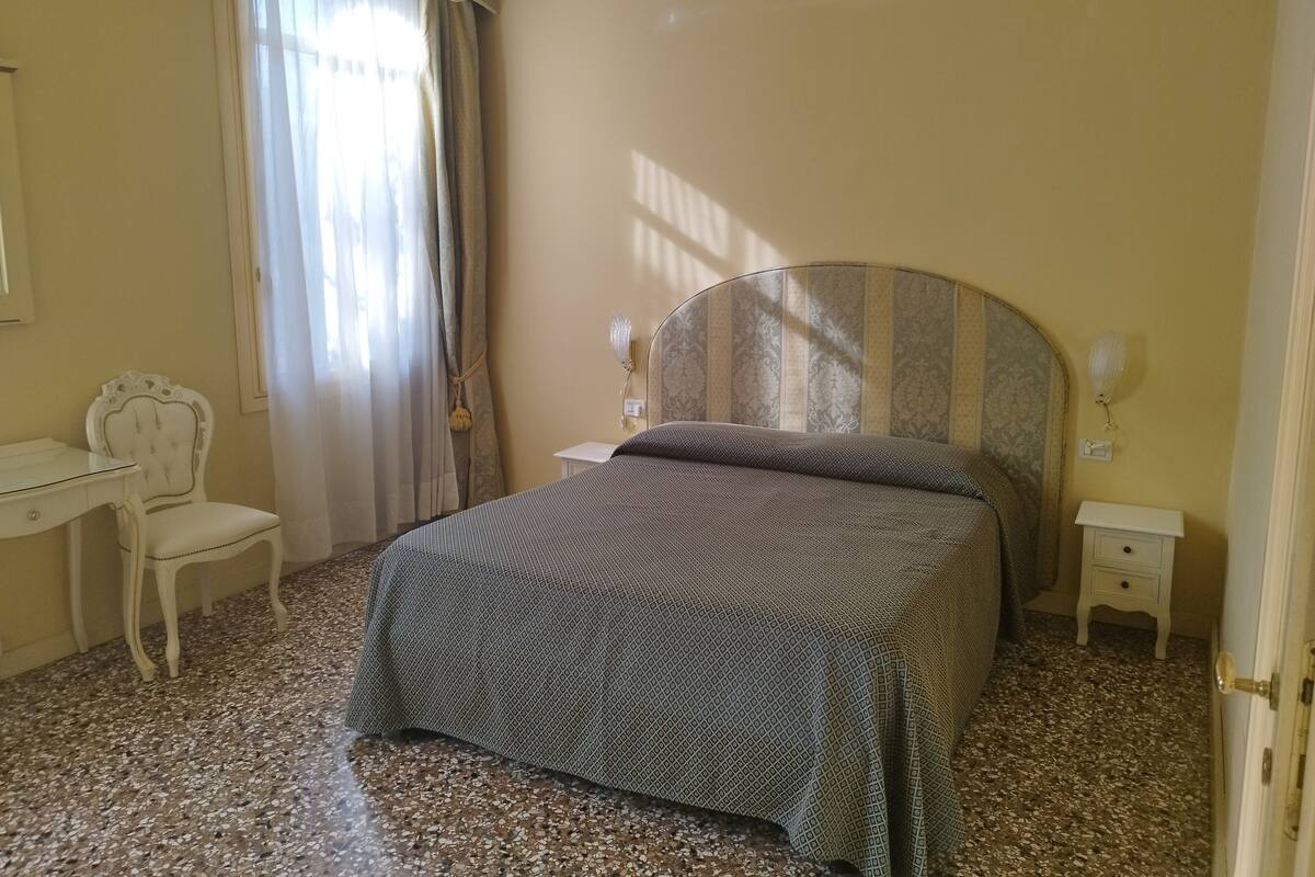 A bedroom with a bed, a chair, a desk, and a nightstand.