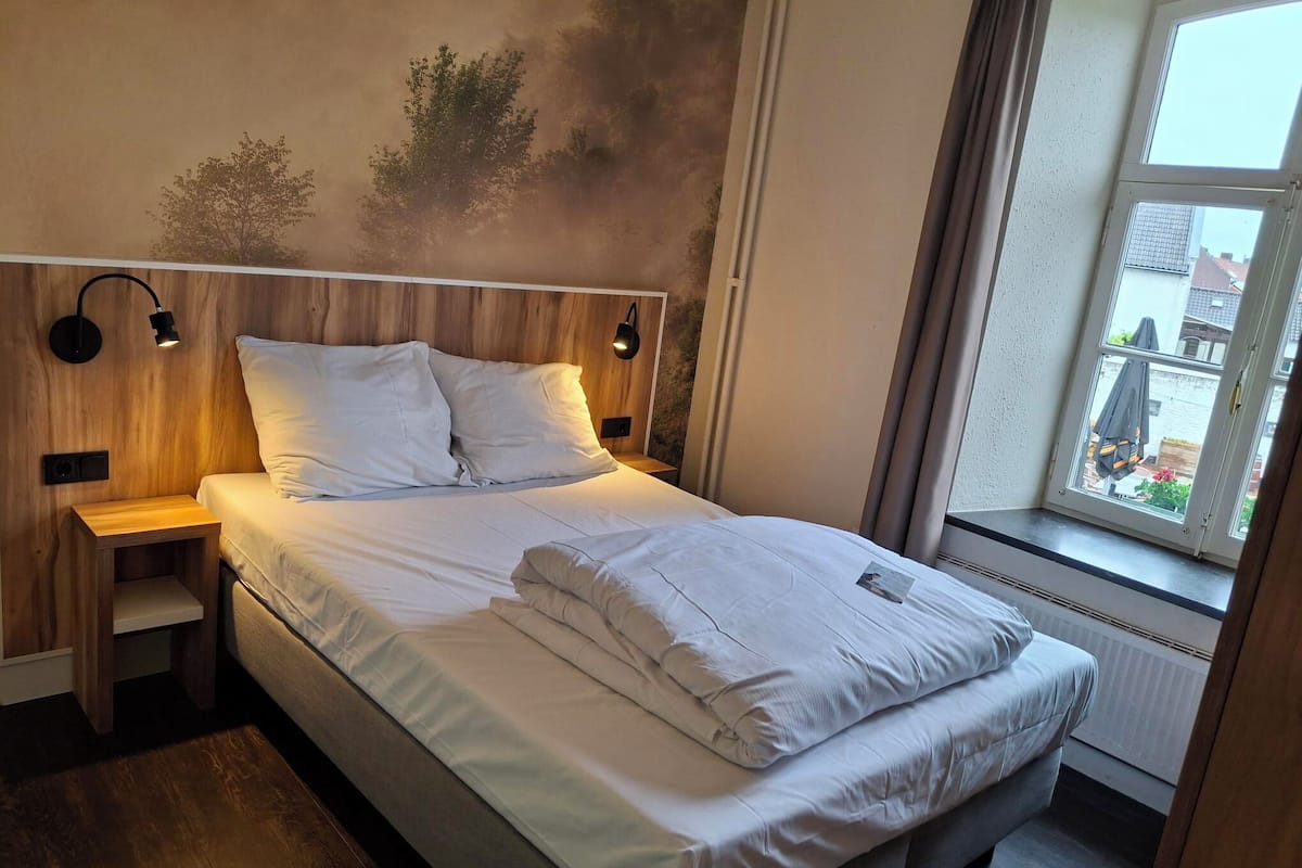 Een net opgemaakt bed met witte lakens, een houten hoofdbord en twee bedlampjes.