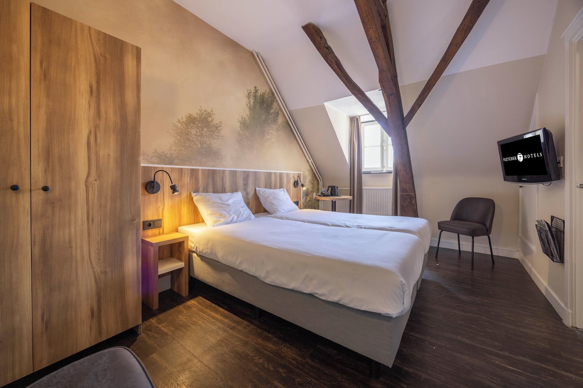 Een slaapkamer met een houten garderobe, een bed met witte lakens, een televisie aan de muur en uitzicht op de omgeving.