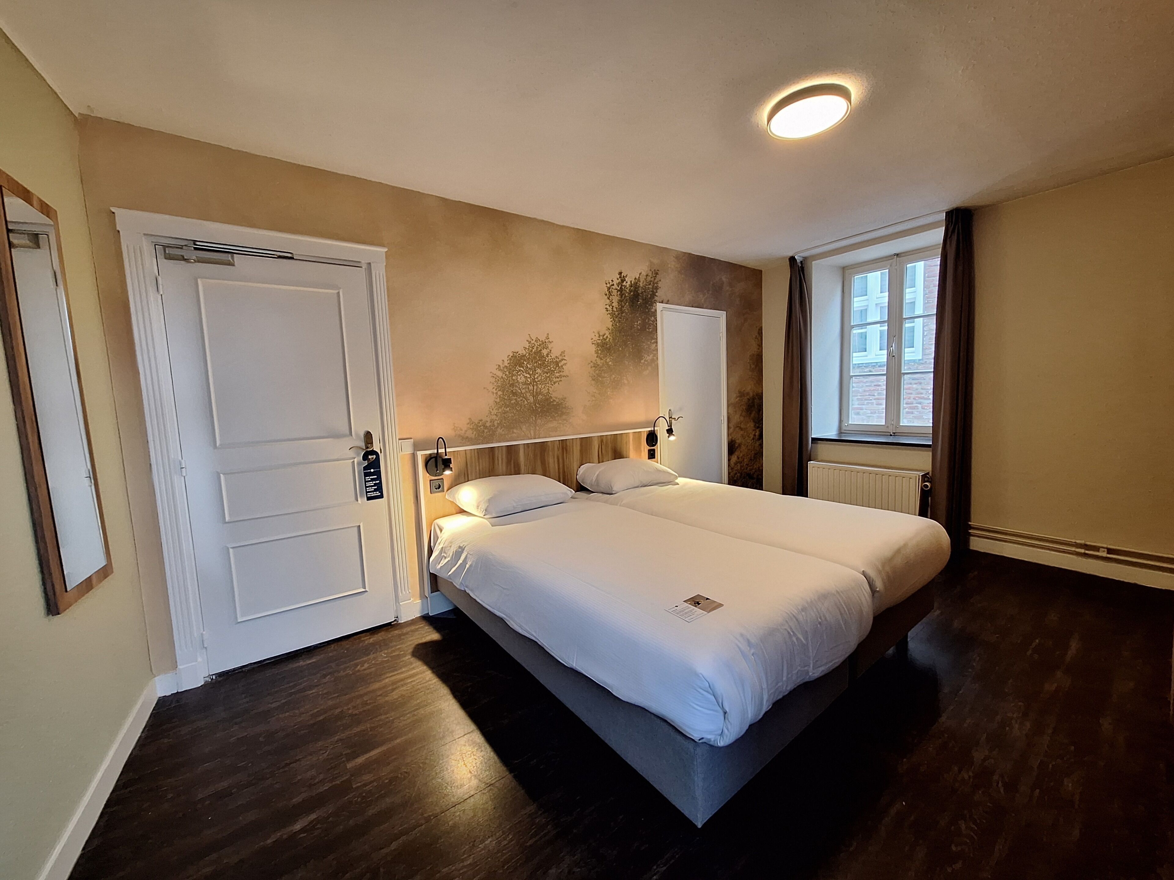 Een slaapkamer met een bed, een deur, een raam en een wandlamp.