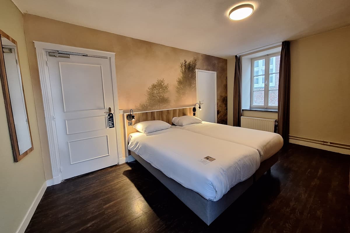 Een slaapkamer met een bed, een deur, een raam en een wandlamp.