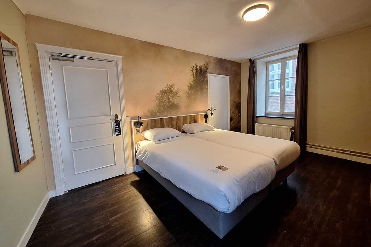 A bedroom with a bed, a door, a window, and a wall-mounted light fixture.
