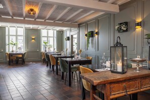 Een eethoek met meerdere tafels en stoelen, een houten bank en een lantaarn op tafel.