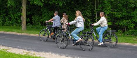 Four people riding bicycles on a paved path with trees in the background.