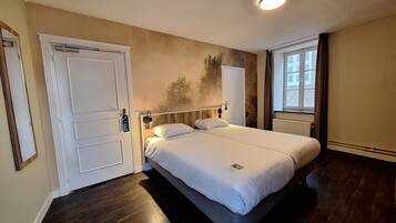 A bedroom with a bed, a door, a window, and a wall-mounted light fixture.