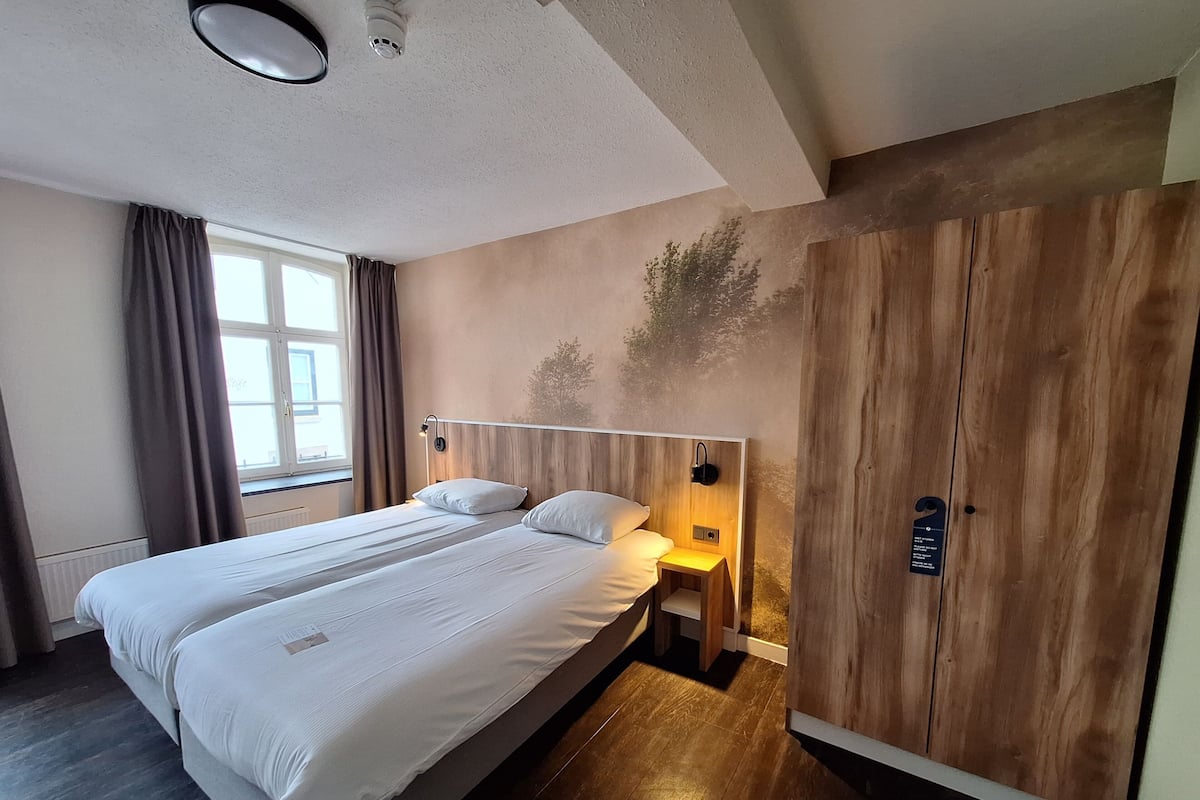 Een hotelkamer met een groot bed, een nachtkastje, een houten garderobe en een raam met gordijnen.