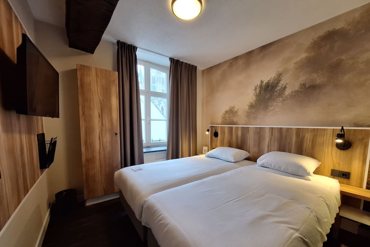 Een hotelkamer met een tweepersoonsbed, een houten hoofdbord, een wandtelevisie en een raam met gordijnen.