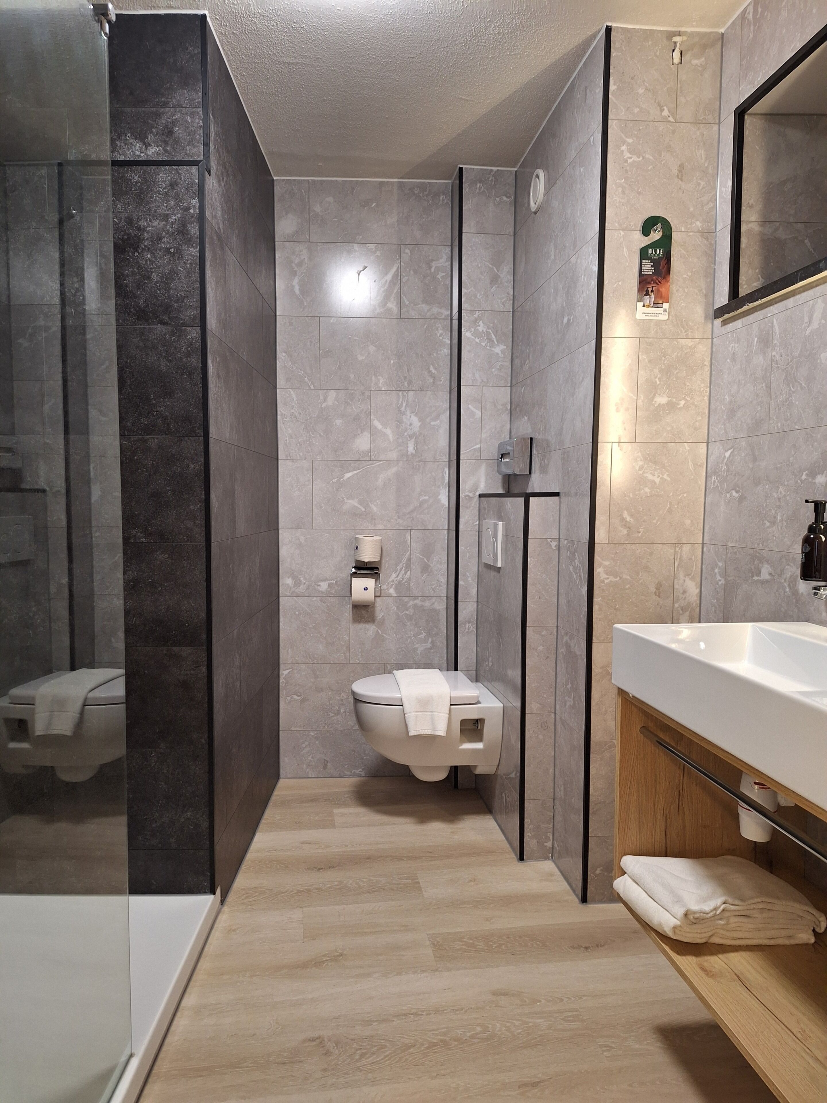 Een moderne badkamer met een douchecabine van glas, een toilet, een wastafel met houten meubel en een spiegel.