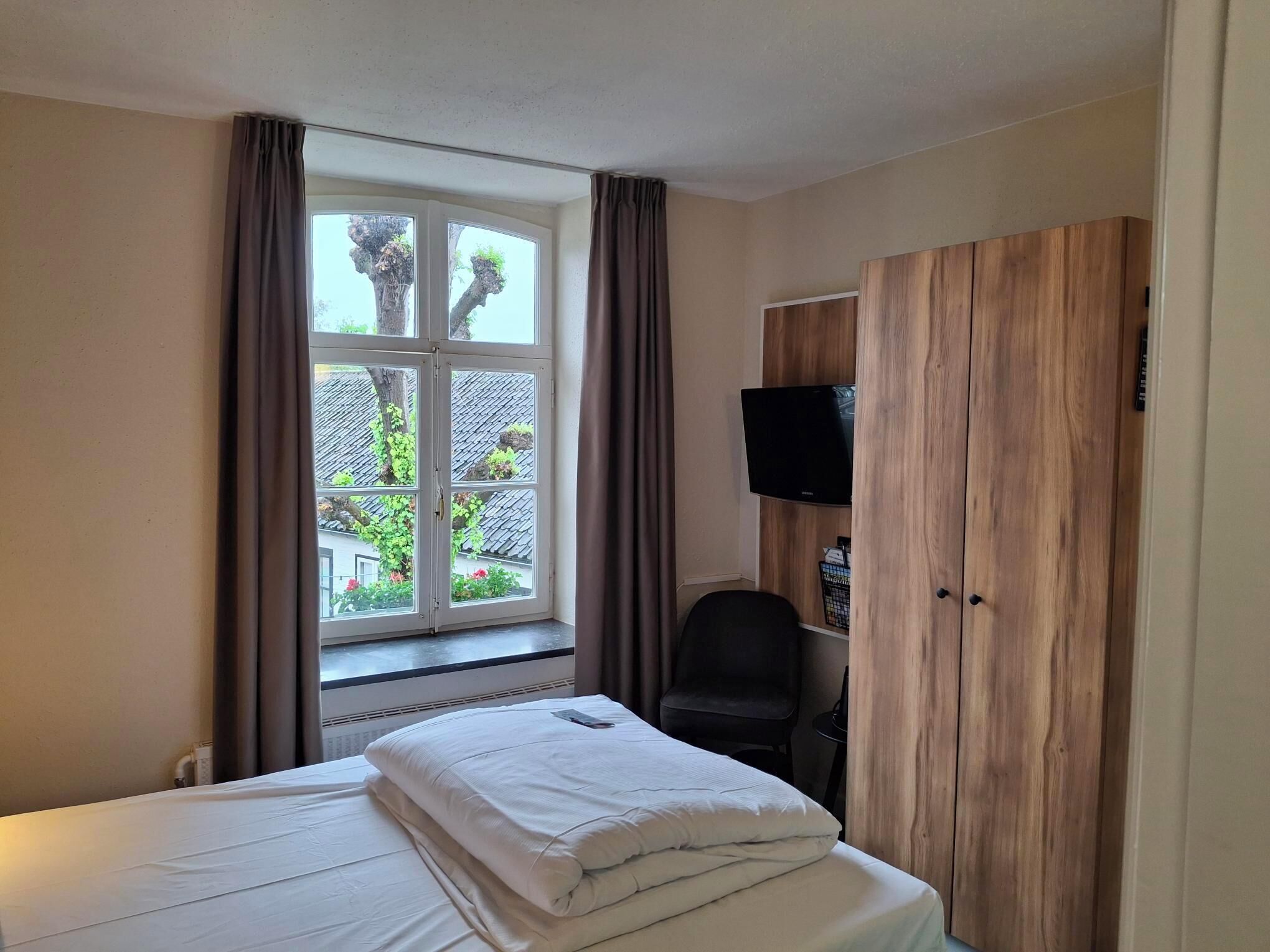 A hotel room with a bed, a television, a wardrobe, and a window with curtains.