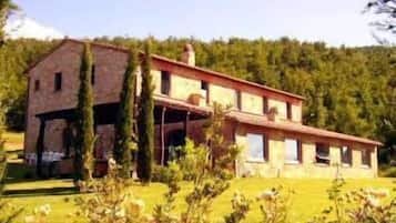 Una casa a due piani con tetto spiovente, immersa nel verde e circondata da alberi.