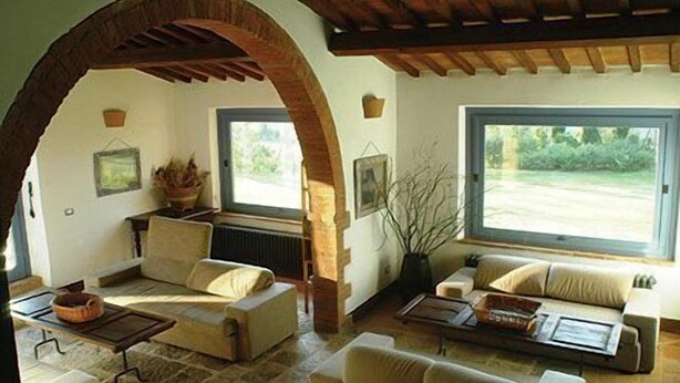 A cozy living room with a stone floor, a wooden ceiling, and large windows offering a view of the outdoors. - Podere Monti (Montepulciano)